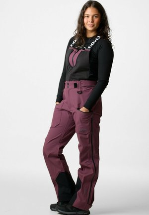 Bordeaux skibroek met zwarte accenten, verstelbare banden, twee zijzakken en een ritssluiting aan de voorkant. Gemaakt van duurzaam, weerbestendig materiaal.