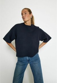 Námořnický oversized pletený svetr s krátkými rukávy, kulatým výstřihem a texturovaným povrchem, kombinovaný se světle modrými džíny.
