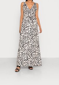 Robe maxi beige avec un motif abstrait noir, présentant un décolleté en V, un design sans manches, une taille cintrée et une texture fluide et lisse.