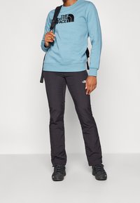 Felpa azzurro chiaro con logo nero, abbinata a pantaloni leggeri neri. Scarponcini da trekking neri completano l'outfit. Design semplice e funzionale.
