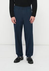 Παντελόνια σε ναυτικό μπλε χρώμα με εφαρμοστή γραμμή, κατασκευασμένα από λείο ύφασμα, με εμπρόσθιο κλείσιμο με κουμπί, επίπεδη μπροστινή όψη και τσέπες.