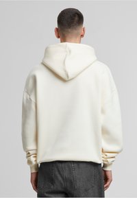Weiße Kapuzensweatjacke mit lässiger Passform, übergroßen Ärmeln und gerippten Bündchen, kombiniert mit dunkelgrauen strukturierten Hosen.