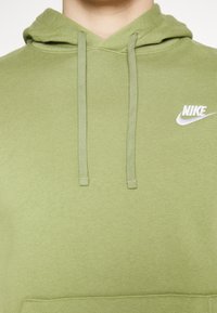 Grön Nike-hoodie med justerbar huva och dragsko, tillverkad av texturerat tyg. Har en vit Nike-logga på bröstet. Enkel, tröja utan knäppning.