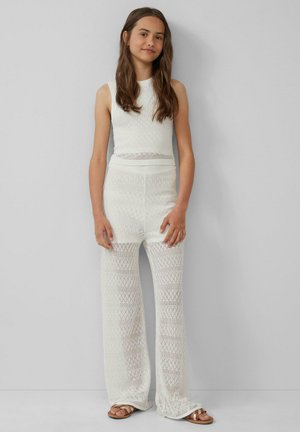 Ensemble en tricot blanc composé d'un top sans manches et d'un pantalon à jambe large avec un motif en losanges. Porté avec des sandales plates.