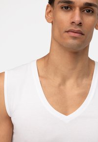 Witte katoenen tanktop met een V-hals ontwerp, met een gladde textuur en schone randen, die een minimalistische stijl benadrukt.