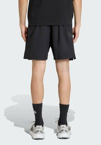 Čierne športové šortky z ľahkého materiálu, s bočnými vreckami, voľným strihom a hladkou textúrou. Nosené s čiernymi ponožkami a teniskami.