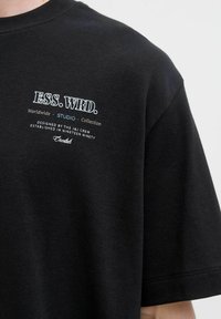 Black cotton t-shirt featuring a centered graphic with "ESS. WRD." and additional text, short sleeves, and a standard fit.