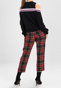 Kvinna i en svart kallaxeltröja med randiga detaljer och röd, svart, vit rutiga byxor, matchat med svarta högklackade ankelstövlar.