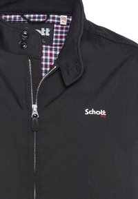 Must svart jakk, millel on tõmblukk ja kaks nupu sulgemist krae peal. Sisemus on kaunistatud lilla ja valge ruudulise mustriga. Tikkitud logo.