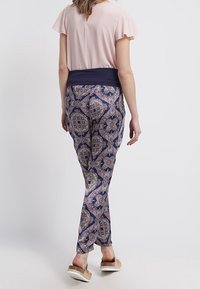 Navy patterned pants with a floral design, mid-rise waist, paired with a light pink top and flat sandals. Smooth fabric, soft texture, slim fit.