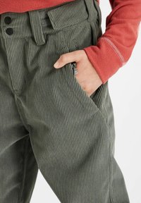 Pantaloni in velluto a coste verde scuro con coste fini, dotati di due bottoni in vita e di una tasca laterale evidenziata da un cordino.