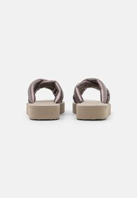 Des sandales slip-on métalliques rose avec une sangle rembourrée et une épaisse semelle beige. Le design présente un dessus texturé et un footbed plat.