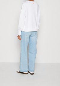 White sweatshirt with a relaxed fit and ribbed cuffs, paired with light blue wide-leg jeans. Subtle logo detail at the back.