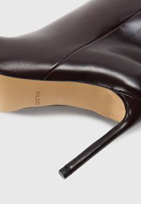 Pantof de piele maro cu toc înalt, cu vârf ascuțit, textură netedă și toc subțire de tip stiletto; talpa interioară poartă numele mărcii "ALDO."
