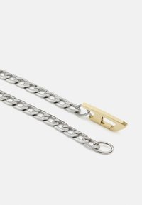Zilveren ketting met ovale schakels, voorzien van een stijlvolle gouden sluiting. De ketting heeft een gestructureerde afwerking, die het gedetailleerde ontwerp benadrukt.