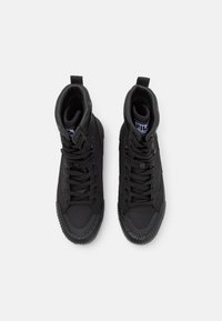 Baskets montantes noires avec une semelle en caoutchouc texturée, une tige synthétique lisse et un design à lacets bien visible. Comprend une boucle au talon pour un enfilage facile.