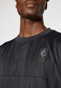 NBA logo sweatshirt in black, featuring a textured striped design and a crew neckline. The logo is rubberized and placed on the chest.