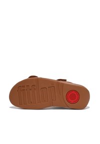 FitFlop sandala podplat, rjava guma z teksturiranimi elementi, vtisnjenim imenom blagovne znamke in rdečim okroglim poudarkom v središču. Raven, širok dizajn.