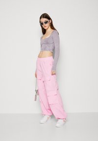 Fialová dlouhá rukávová crop top s texturovaným materiálem, spárovaná s nadměrnými růžovými cargo kalhotami s bočními kapsami a elastickým pasem.