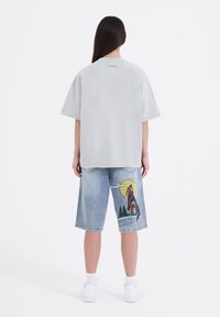 Camiseta de gran tamaño en gris claro con cuello redondo, combinada con pantalones cortos de mezclilla que presentan un gráfico colorido de un lobo y el texto "NACIDO PARA SER SALVAJE."