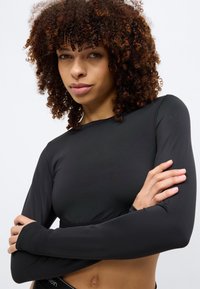 Μαύρο crop top με μακριά μανίκια από απαλό, ελαστικό ύφασμα. Διαθέτει στρογγυλή λαιμόκοψη και εφαρμοστή γραμμή που αναδεικνύει τα χέρια του μοντέλου.