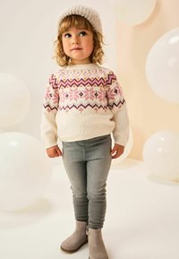 Strikket cremefarvet sweater med pink og lilla Fair Isle mønster, parret med grå slim-fit jeans og beige ankelstøvler. Inkluderer også en strikket hue.