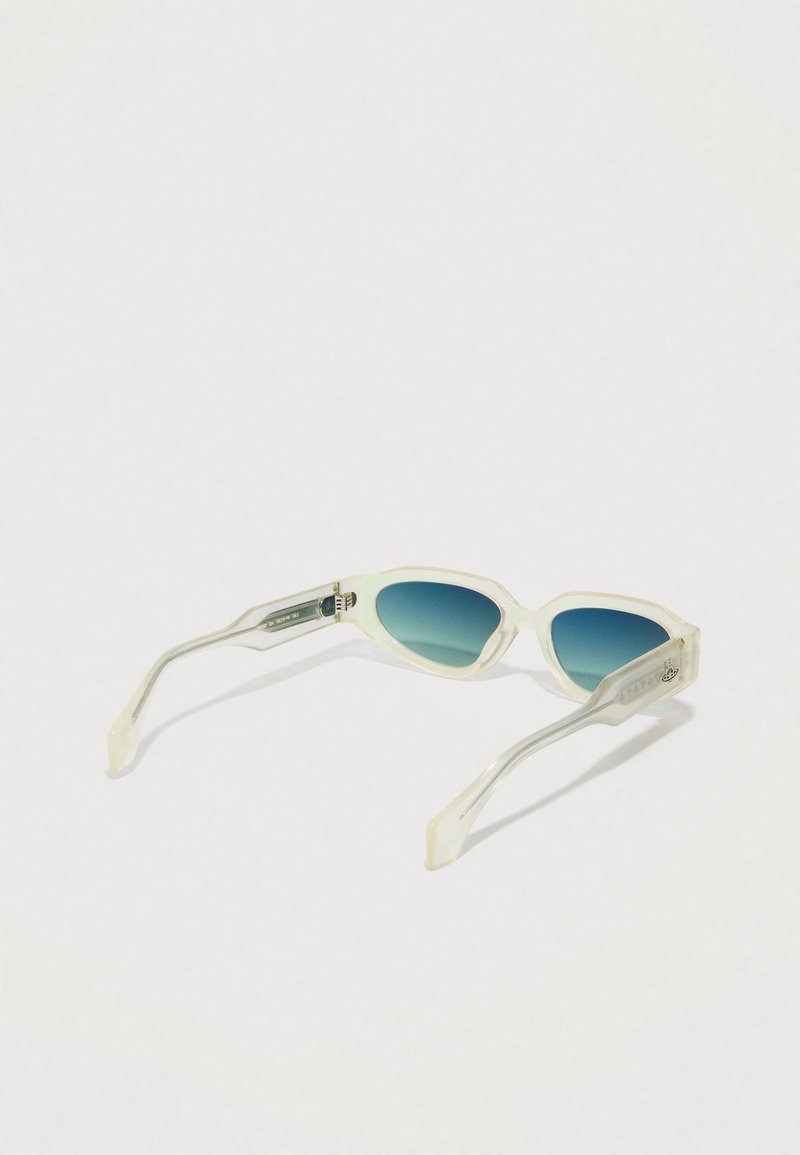Sunglasses with a translucent cream frame and graduated blue lenses, featuring slender arms and subtle branding on the temple.
