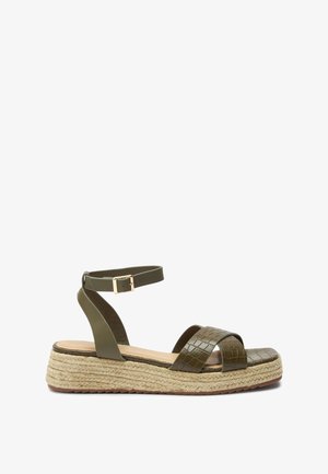 Sandale verte en cuir synthétique avec une texture embossée croco, deux brides et une boucle réglable à la cheville, sur une semelle compensée enveloppée de jute.
