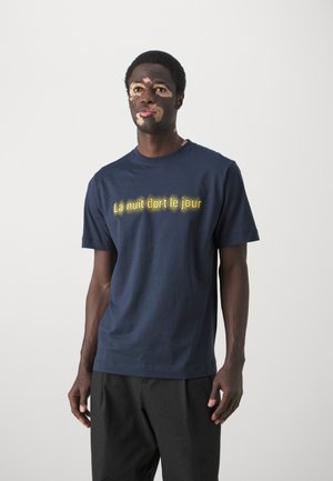 Marineblå bomulds t-shirt med korte ærmer og rund hals, med gule trykte bogstaver "La nuit dort le jour" i en lysende effekt.