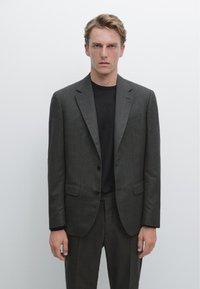 Completo grigio su misura con sottile trama, design monopetto, due bottoni e rever a incrocio, abbinato a una maglietta nera a girocollo.