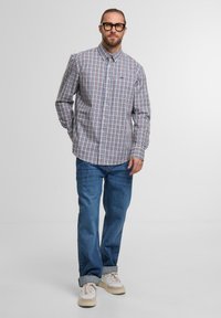 Ein kariertes Button-up-Hemd in vielen Farben aus Baumwolle, kombiniert mit hellblauen Jeans und beigen Sneakers.