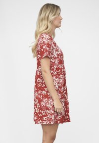 Punainen kukkakuvioinen mekko, jossa on lyhyet hihat, istuva yläosa ja liehukehelmainen hame. Kuosissa on valkoisia ja vaaleanpunaisia kukkia teksturoidulla kankaalla.