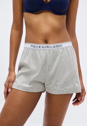 Ženski torzo s tamnoplavim grudnjakom i svijetlosivim šorcama Polo Ralph Lauren s bijelim pojasom s logom na jednobojnoj pozadini.