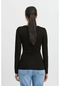 Black long-sleeve top with a form-fitting design, featuring a round neckline and smooth texture, paired with light blue denim jeans.