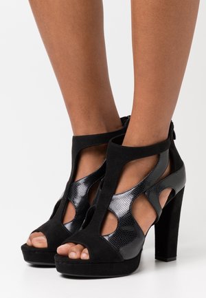 Chaussures à talons hauts noires avec des accents en daim et en cuir laqué texturé. Design découpé avec bout ouvert et semelle plateforme. Fermeture éclair à l'arrière.