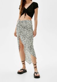 Musta ribbed crop toppi lyhyillä hihoilla, yhdistettynä valkoiseen kukkakuosisesta kietaisuhameeseen, jossa on sivuaukko ja mustat narukengät.