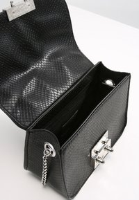 Svart texturerad handväska med reptilmönster, silverdetaljer, kedjestrap och ett innerfack med dragkedja. Öppningen i toppen visar de inre facken.