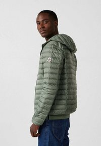 Giacca imbottita verde con cappuccio, caratterizzata da una texture trapuntata verticale, una toppa logo sulla manica e un design aderente.