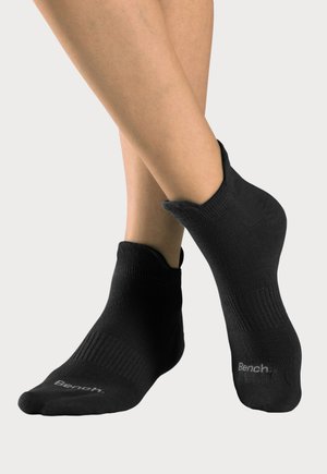 Füße mit schwarzen, niedrig geschnittenen Socken der Marke Bench, ein Fuß leicht angehoben, um Details und Textur der Socke zu zeigen.