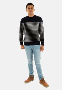 Maglione a righe navy con linee orizzontali color crema, scollo a girocollo e dettagli con bottoni sulla spalla, abbinato a jeans chiari e stivali marroni.