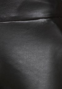 Matériau en simili cuir noir avec une surface texturée, présentant une couture visible et un léger brillant, mettant en valeur une apparence lisse et mate.