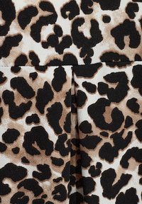 Leopardmönstrad tyg med en strukturerad yta i svart, brunt och krämfärgat, som visar en vikt sektion i botten.