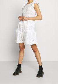 Vit klänning i ögonfransar med volangärmar, lagerdelt skör och utskuret mönster. Matchad med svarta snörboots för kontrast.