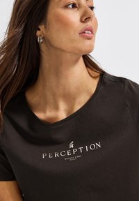 Černé tričko vyrobené z měkké látky s kulatým výstřihem a stříbrným potiskem loga s nápisem "PERCEPTION MODERN VIBES DAILY."