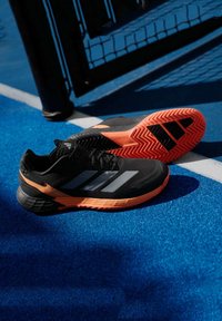 Μαύρα αθλητικά παπούτσια με πορτοκαλί και γκρί λεπτομέρειες, διαθέτοντας υφή στο πάνω μέρος, καουτσούκ σόλα και ζιγκ-ζαγκ μοτίβο στη σόλα.