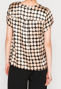 Kortärmad topp i beige satin med ett svart geometriskt mönster. Rund halsringning och avslappnad passform, med en ryggparti detalj.