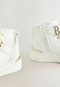 Hvide high-top sneakers med en blank guldaccent, der har sideskaber og præget bogstavdetalje på ankelen. Glat, syntetisk materiale.