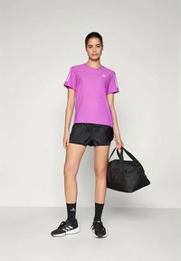 Violet sporta kreklis ar īsām piedurknēm, melni šorti, melnas sporta kurpes un melna sporta soma; gluda auduma, vienkāršs dizains.