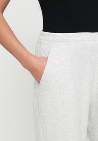 Jasnoszare spodnie dresowe charakteryzują się zwężanym krojem, miękką fakturą i elastycznym pasem. Po lewej stronie widoczna jest boczna kieszeń.