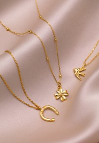 Trois colliers en or avec un fer à cheval, un charme floral et un pendentif en forme d'oiseau sur un fond en satin doux. Les chaînes incluent de petites perles.
